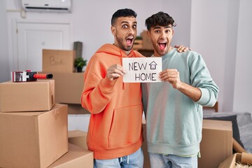 Young hispanic gay couple moving to a new home celebrating crazy and amazed for success with open...