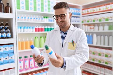 Young hispanic man pharmacist smiling confident holding medication bottles at pharmacy