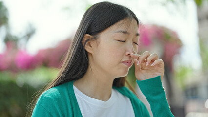 Fototapeta premium Young chinese woman looking to the side sneezing at park