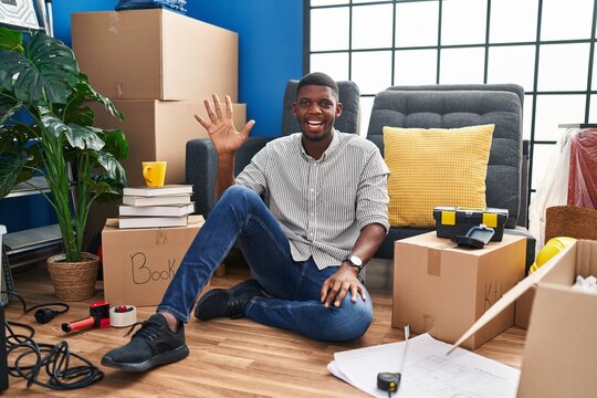 African american man sitting on the floor at new home showing and pointing up with fingers number five while smiling confident and happy.