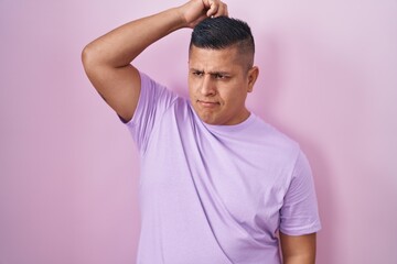Young hispanic man standing over pink background confuse and wondering about question. uncertain with doubt, thinking with hand on head. pensive concept.