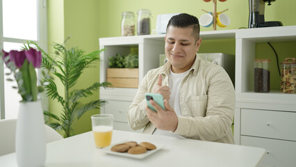 Young hispanic man using smartphone having breakfast at dinning room