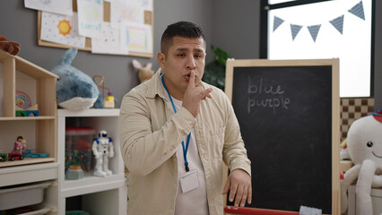 Young hispanic man preschool teacher asking for silence at kindergarten