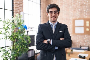 Young hispanic man business worker standing with arms crossed gesture at office