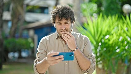 Young hispanic man watching video on smartphone concentrated at park