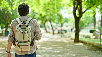 Young hispanic man tourist wearing backpack walking backwards at park