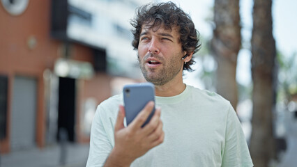 Young hispanic man smiling confident having free hands call at street