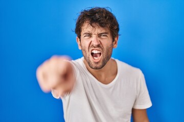 Fototapeta na wymiar Hispanic young man standing over blue background pointing displeased and frustrated to the camera, angry and furious with you