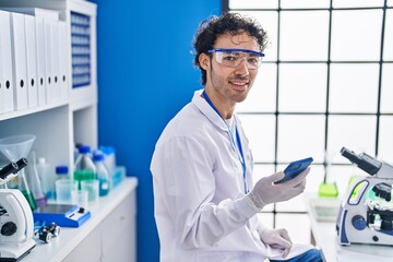 Young hispanic man scientist using smartphone working at laboratory