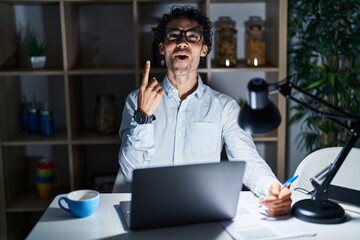 Obraz premium Hispanic man working at the office at night amazed and surprised looking up and pointing with fingers and raised arms.