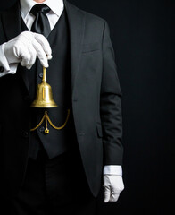 Portrait of Butler or Hotel Concierge in Dark Suit and White Gloves Holding a Gold Bell. Ring for Service Concept. - obrazy, fototapety, plakaty