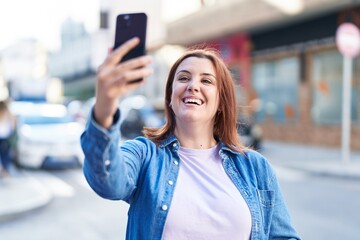 Young beautiful plus size woman smiling confident making selfie by the smartphone at street