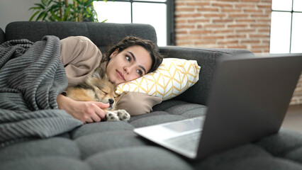 Young hispanic woman with dog watching movie lying on sofa at home
