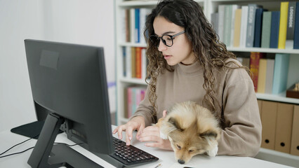 Young hispanic woman with dog student using computer studying at library university