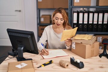 Young woman ecommerce busines worker writing on notebook holding package at office