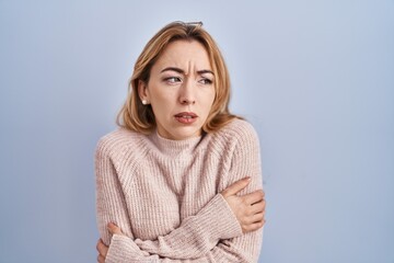 Hispanic woman standing over blue background shaking and freezing for winter cold with sad and...