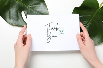 Inscription thank you on paper in hands with big green leaves on white background