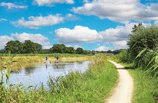 Beautiful dutch rural landscape, river Aa with stand up paddlers, empty riverside hiking and cycle trail - Heeswijk, Noord-Brabant, Netherlands