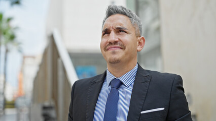 Young hispanic man business worker standing with serious face at street