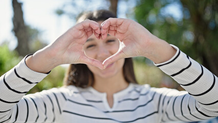 Young beautiful hispanic woman smiling confident doing heart gesture with hands at park