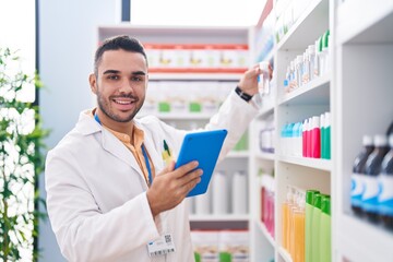 Fototapeta premium Young hispanic man pharmacist using touchpad working at pharmacy