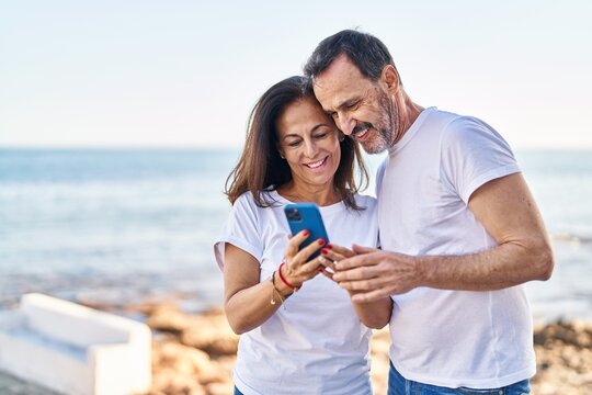 Middle age man and woman couple using smartphone standing together at seaside