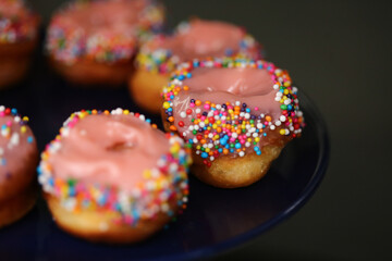Donuts de creme cor-de-rosa cobertos com confetes coloridos, uma delícia irresistível na mesa de doces da festa infantil.