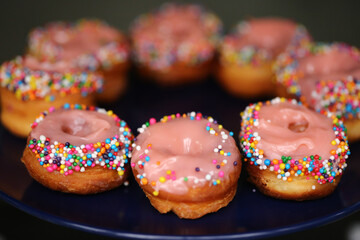 Donuts de creme cor-de-rosa cobertos com confetes coloridos, uma delícia irresistível na mesa de doces da festa infantil.