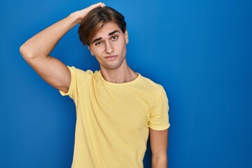 Young man standing over blue background confuse and wonder about question. uncertain with doubt, thinking with hand on head. pensive concept.