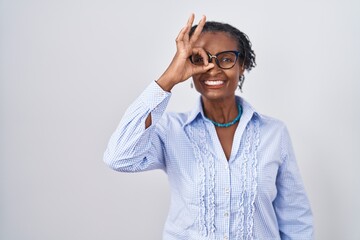 African woman with dreadlocks standing over white background wearing glasses doing ok gesture with hand smiling, eye looking through fingers with happy face.