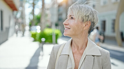 Middle age blonde woman smiling confident looking to the sky at street