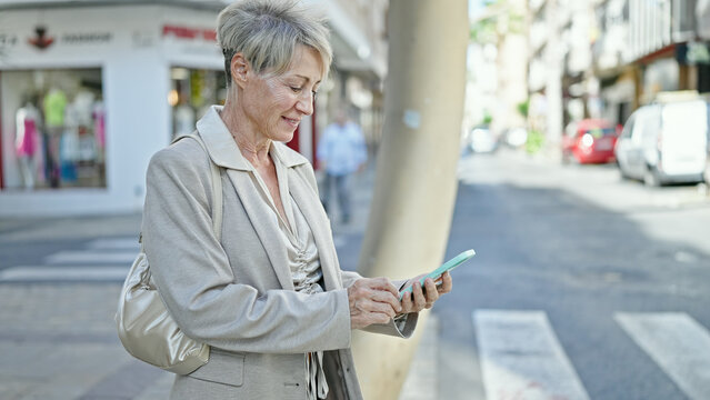 Middle age blonde woman smiling confident using smartphone at street