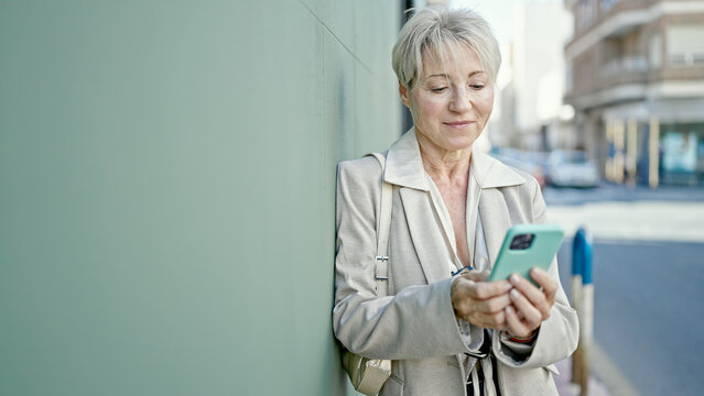 Middle age blonde woman smiling confident using smartphone at street