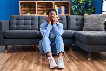 African american woman listening to music sitting on floor at home