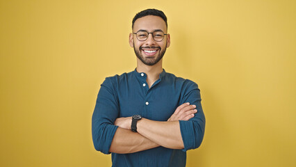 Young hispanic man standing with arms crossed gesture over isolated yellow background