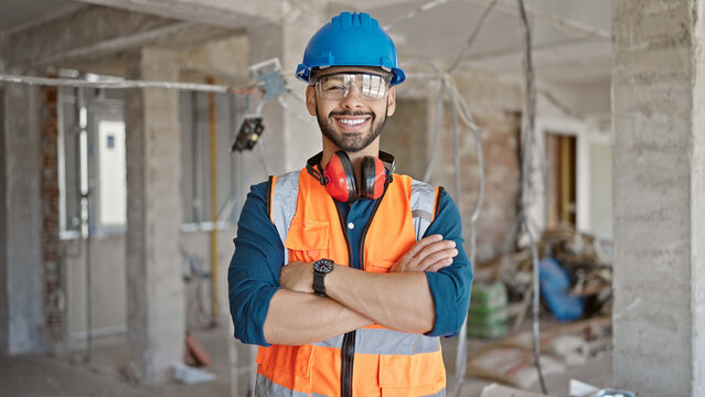 Young hispanic man builder smiling confident with crossed wearing hardhat at construction site