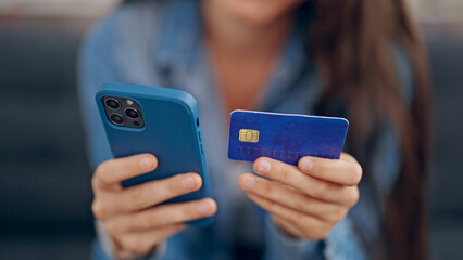 Young beautiful hispanic woman shopping with smartphone and credit card sitting on sofa at home