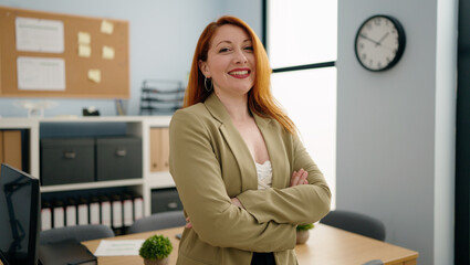 Young redhead woman business worker standing with arms crossed gesture at office
