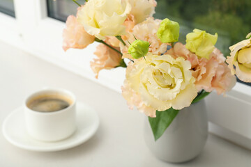 A pot of coffee and a vase of flowers on the windowsill with a view of the city