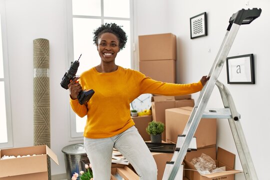 African American Woman Holding Drill Standing On Ladder At New Home