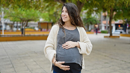 Young pregnant woman smiling confident touching belly at park