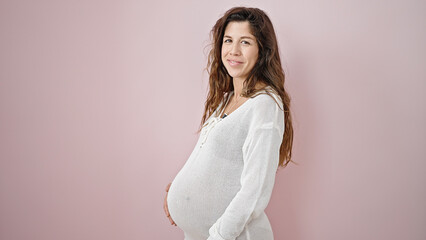 Young pregnant woman smiling confident touching belly over isolated pink background