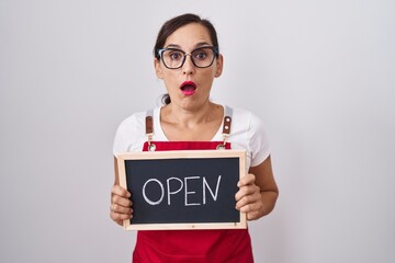 Middle age brunette woman holding banner with open text scared and amazed with open mouth for...
