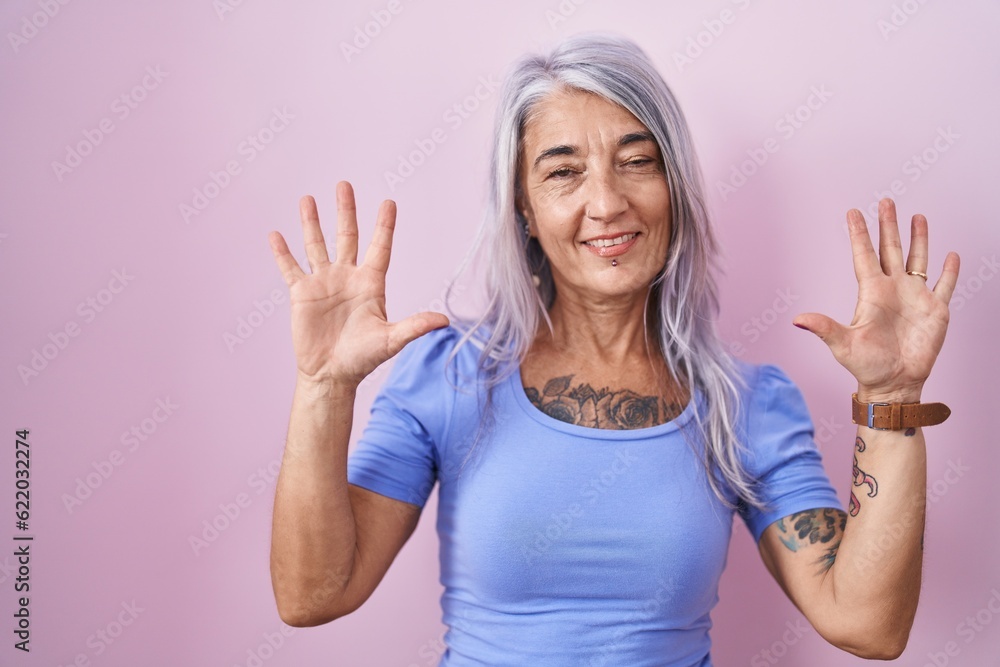 Wall mural middle age woman with tattoos standing over pink background showing and pointing up with fingers num