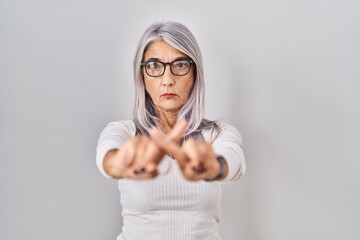 Middle age woman with grey hair standing over white background rejection expression crossing...