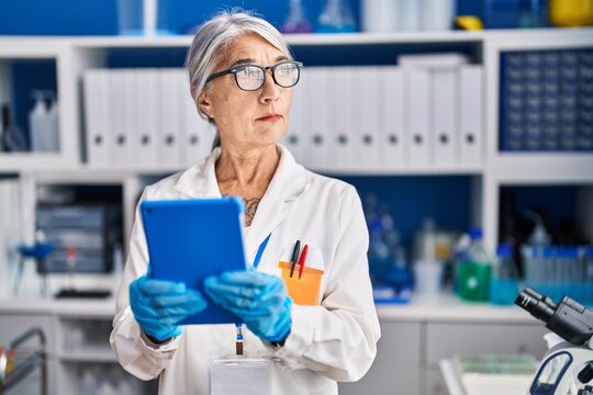 Middle age grey-haired woman scientist using touchpad working at laboratory