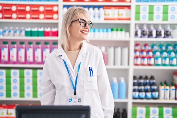 Young caucasian woman working at pharmacy drugstore looking away to side with smile on face, natural expression. laughing confident.