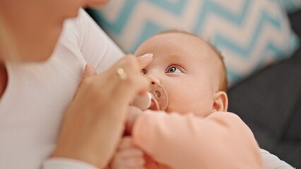 Mother and daughter sitting on sofa sucking pacifier at home