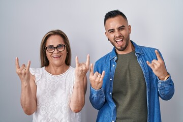 Hispanic mother and son standing together shouting with crazy expression doing rock symbol with hands up. music star. heavy music concept.