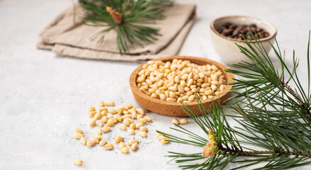 Pine nuts in a bowl  and scattered on a white texture background with branches of pine needles. The concept of natural, organic and healthy superfoods and snacks.
